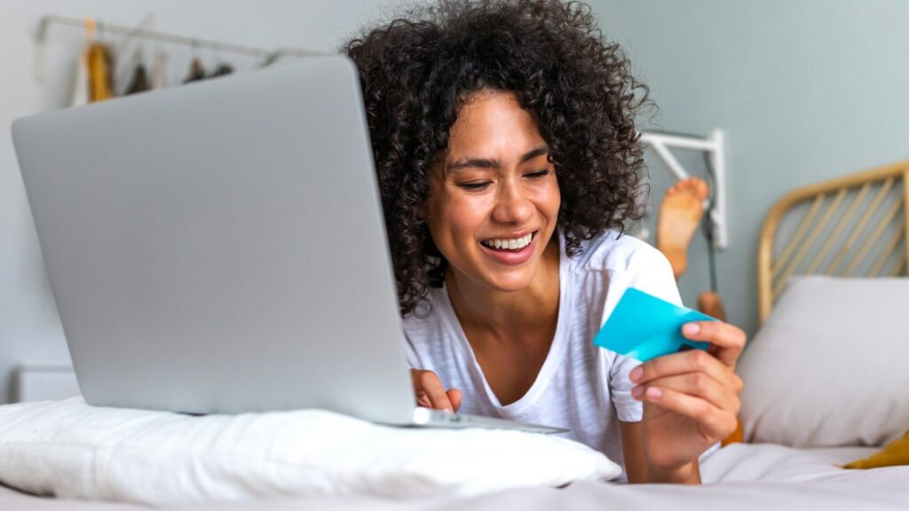 Happy young African American woman online shopping using laptop and credit card on bed in bedroom.  - happy young african american woman online shopping using laptop and credit card on bed in bedroom  1024x576 - Home